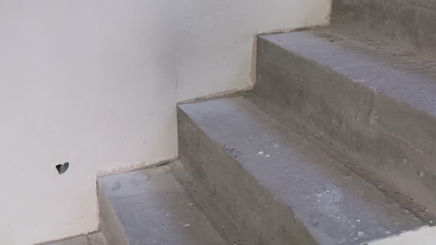Rough gray concrete stairs lead up inside an unfinished building, showing the raw construction materials and the basic structure of a developing space.