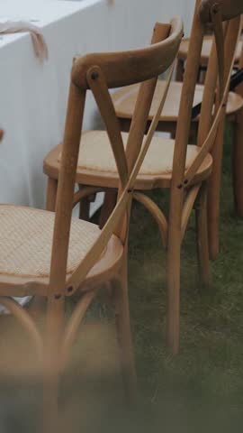 Row of wooden outdoor chairs next to a long table outdoors on green grass. Wedding day, wedding decor, festive dinner or party. Vertical video