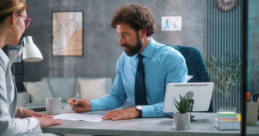 Bank employee manager explains loan options and interest rates to a female client, pointing to documents during a professional financial consultation at the office. Part 19 of the “Dad’s Day” series.