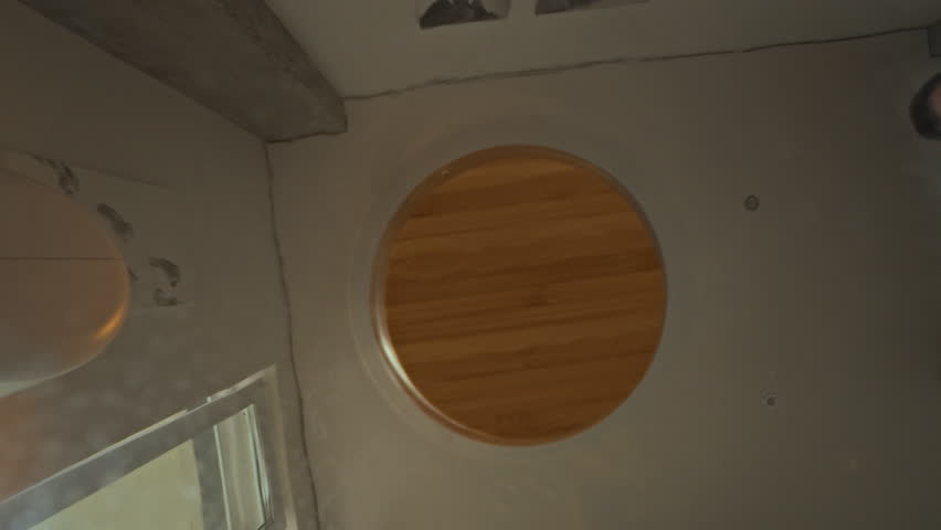 A middle-aged man of European appearance is in the kitchen. He opens a glass jar, lifting the wooden lid, and looks inside. The scene takes place at home, in a domestic setting