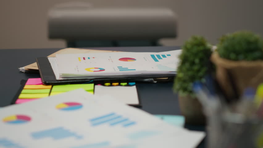 Close up of data insights on papers in startup boardroom at night, charts and forecasting icons displayed on laptop and projection board for a tech savvy approach to business strategy.