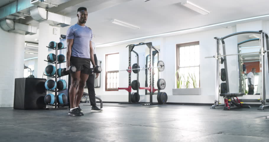 African American trainer cueing client performing dumbbell lunges at gym for muscle gain. Strength training, fitness, exercise, gym, athleticism, motivation, wellness