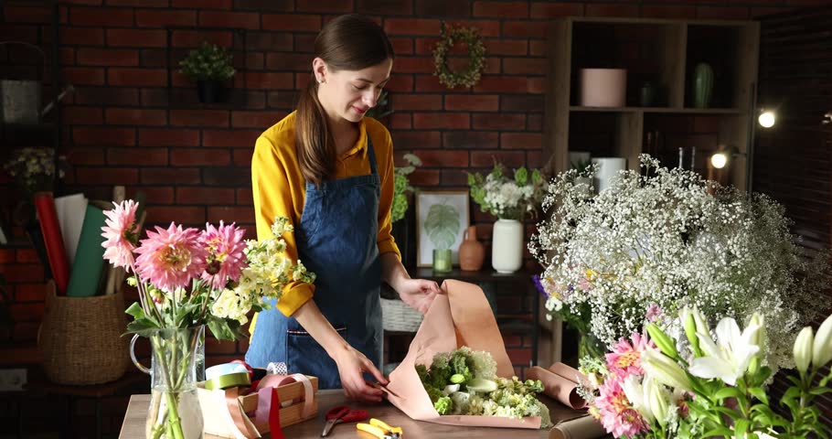 Professional florist making bouquet of flowers at wooden table in shop