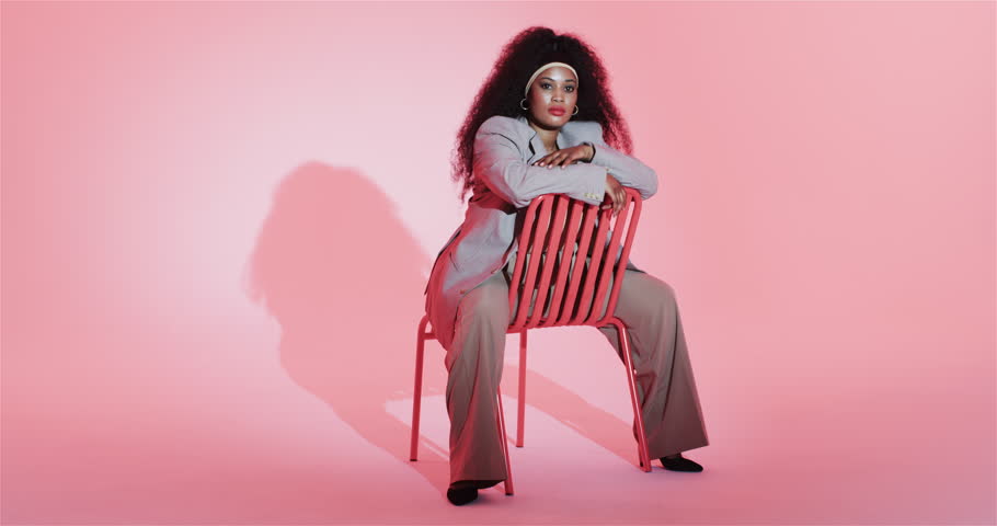 Upon recording African American woman leaning resting on chair backrest for studio shoot smiling. Portrait, fashion, elegance, confidence, studio, minimalist, professional