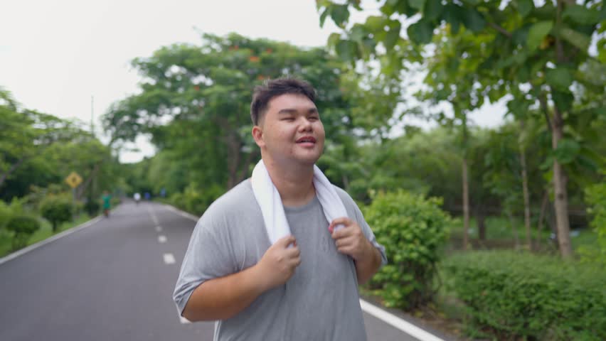 Asian plus-size man exercises outdoors in the garden to lose weight. Attractive young overweight guy spend leisure time on weekend doing running workout to improve health and overall fitness in park.