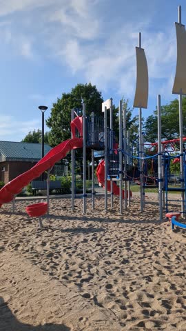 Modern Outdoor Playground with Red Slides and Climbing Structure on Sandy Surface Under Blue Sky