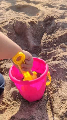 Child Playing with Sand Using Yellow Shovel and Pink Bucket at Playground, Close-Up of Outdoor Activity