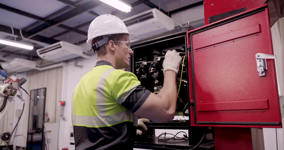male technician performs slowmotion maintenance on industrial electrical cabinet inside smart factory using gloves and safety gear during automation training under industry40 engineering standard