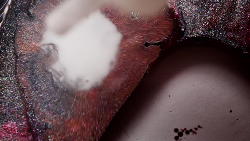 Macro shot of glittery grey and pink inks disturbed by a sudden blast of milky liquid, causing shimmering pigments to scatter.