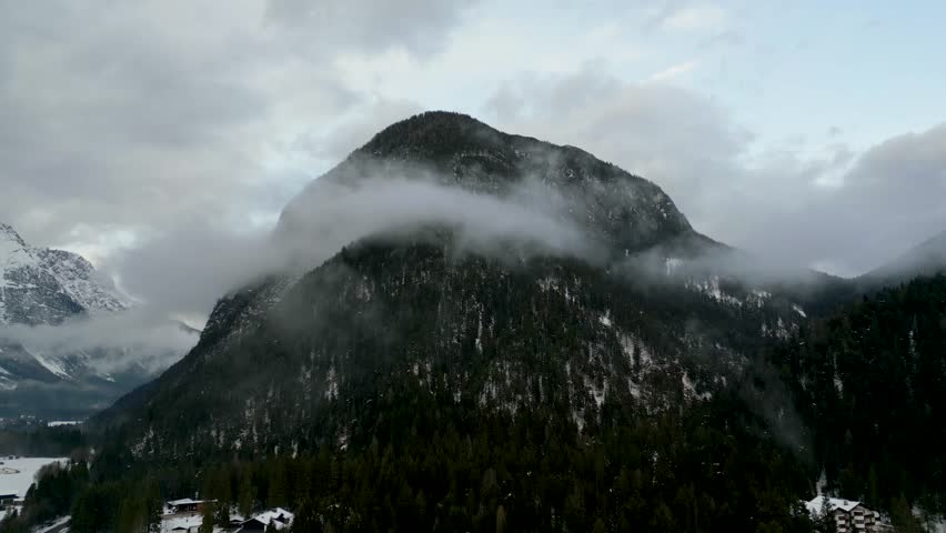 A stunning long shot of a majestic mountain in winter, with natural cloud and fog movement adding a dramatic and serene atmosphere.