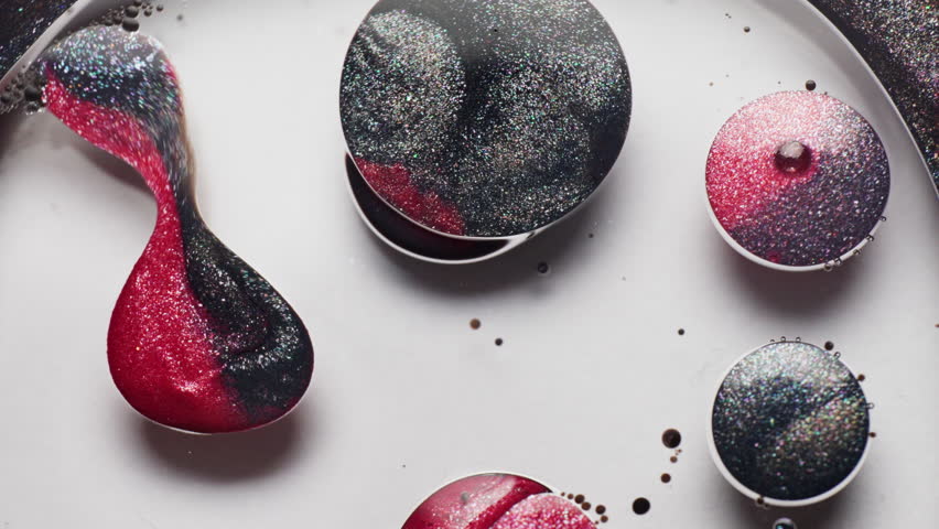 Macro shot of glittery red and black ink droplets suspended in liquid, moving and merging as shimmering pigments swirl inside.