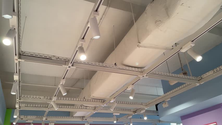 Industrial-style ceiling with exposed ductwork, track lighting, metal framework, and visible piping, showcasing a modern minimalist interior design.