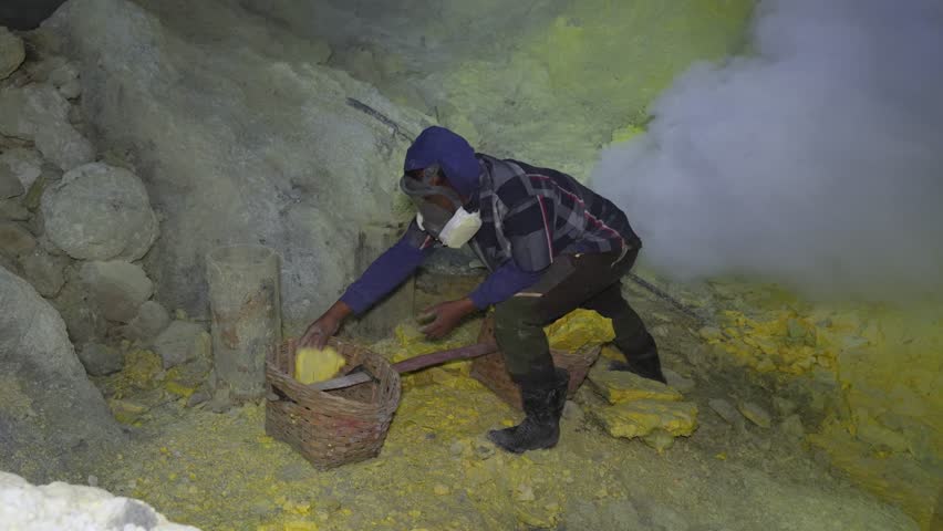 Miner working with sulfur pieces under toxic gas cloud in East Java