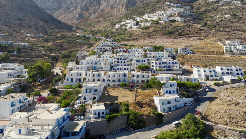Backwards reveal drone shot uncovering the whitewashed village and port of Aegiali on Amorgos island under bright summer skies