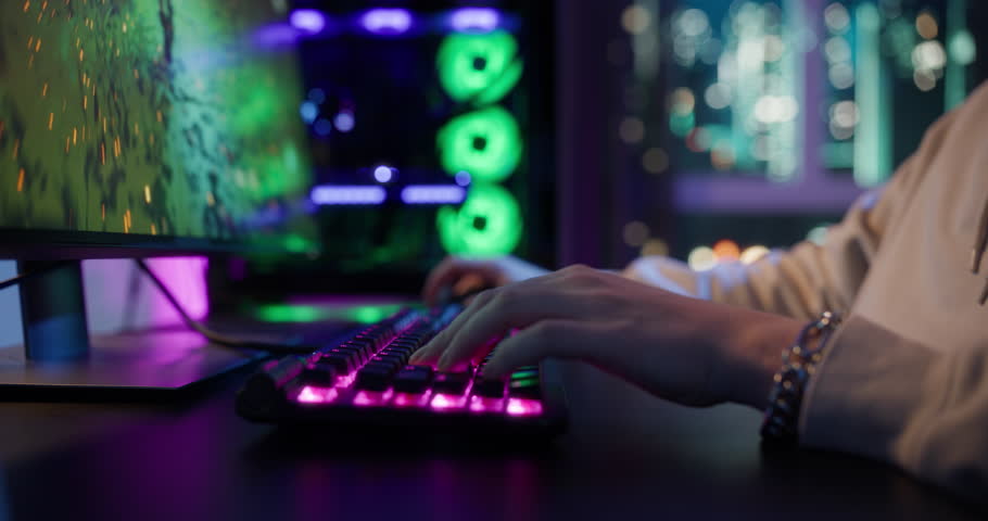 Close Up of Gamer’s Hands Rapidly Pressing Movement Keys on a Glowing RGB Computer Keyboard During Intense Gameplay at Home in a Dark Room. Anonymous Player Playing an Online Shooter Video Game