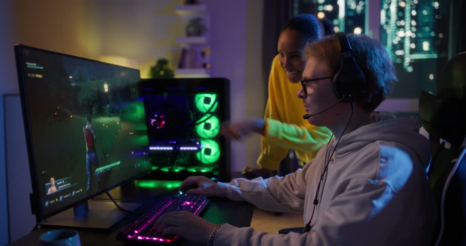 Diverse Young Couple Playing Video Games at Home. Gamer Playing an Online Shooter, Girlfriend Cheering Him On. Caucasian Male and Black Female Giving High Five and Celebrating the Win