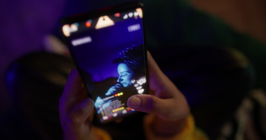 Young Female Sitting on a Bed in Her Gamer Room, Scrolling Through a Video Streaming App, Selecting Influential Content to Watch on Her Smartphone. Rotating Cinematic Robot Camera Movement