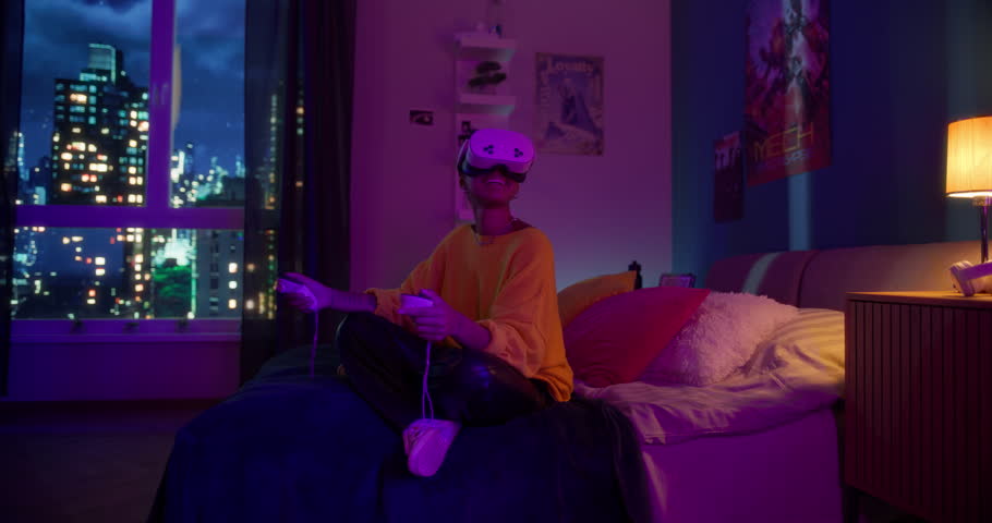 Young Black Woman Sitting on a Bed in a Colorful Neon-Lit Room at Home, Wearing a Virtual Reality Headset, Using Controllers with Her Hands while Exploring a 3D Interactive VR Experience