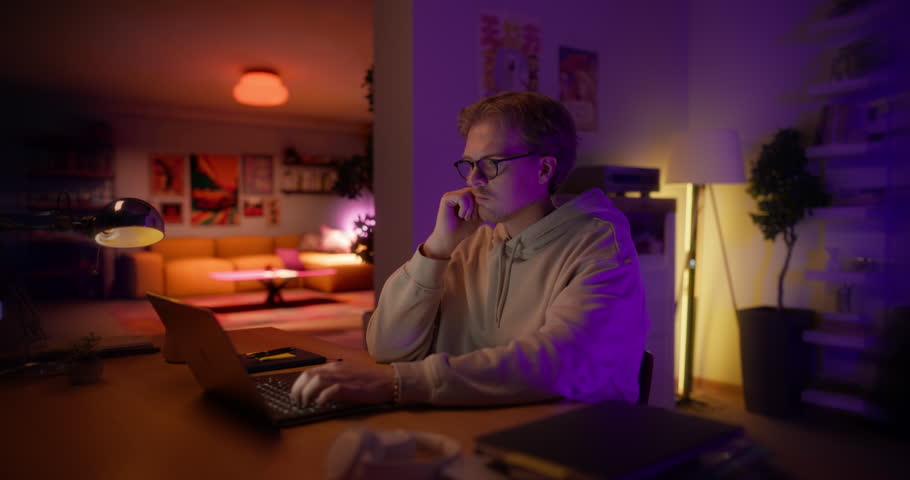 Young Focused Caucasian Man Sitting Behind a Desk at Home, Working on Laptop Computer, Thinking and Problem Solving Tasks. Manager Doing Remote Work or Study for Exams. Static Footage