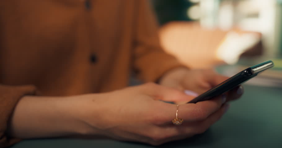 Portrait of a Young Female in a Stylish Cozy Living Room Using Smartphone and Drinking Coffee from a Mug at Home. She is Browsing Internet and Checking Updates on Social Network, Enjoying Her Day