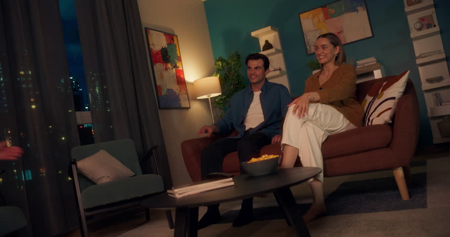 Smiling Couple Sitting on a Couch, Enjoying a Quiet Evening Watching Television and Having Light Hearted Conversation. Small Girl Running to Her Mother and Father, Wanting to Spend Time Together