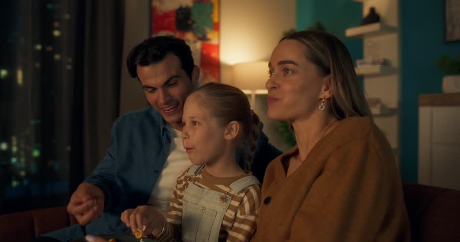 Smiling Couple Sitting on a Couch, Enjoying a Quiet Evening Watching Television and Having Light Hearted Conversation. Small Girl Running to Her Mother and Father, Wanting to Spend Time Together