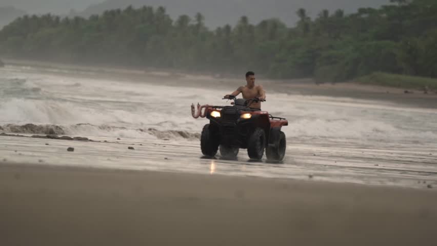 A man rides an ATV quad bike across the wide, sandy shores of a beach in Santa Teresa, Costa Rica.