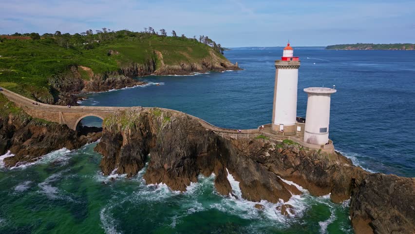 Orbital drone shot from left to right around Petit Minou lighthouse, showing the side path, crashing waves, and rocky cliffs. Brittany in France