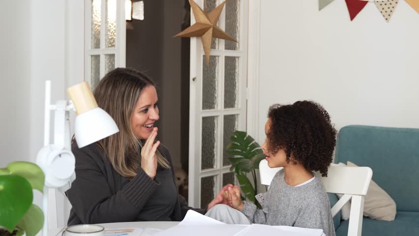 Caucasian mother and African American daughter studying at home, doing homework in cosy white room. Parent teach, child school girl learn knowledge, write exercise read book. Education for children