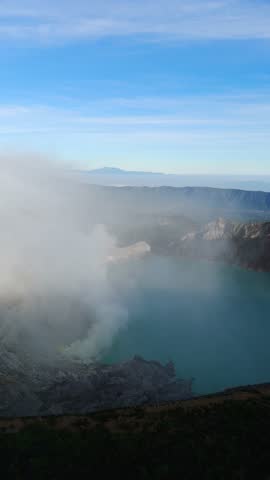 Vertical, aerial: Kawah Ijen volcano with smoke at sunrise in East Java, Indonesia, parallax drone shot