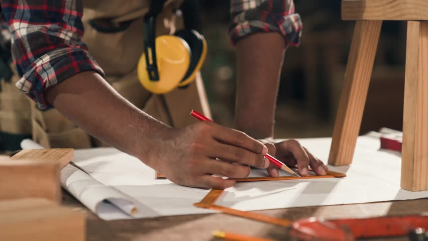 Young African American carpenter designing and building wooden chair at workbench in wood workshop, showcasing craftsmanship, creativity, and hands-on furniture making process with precision.