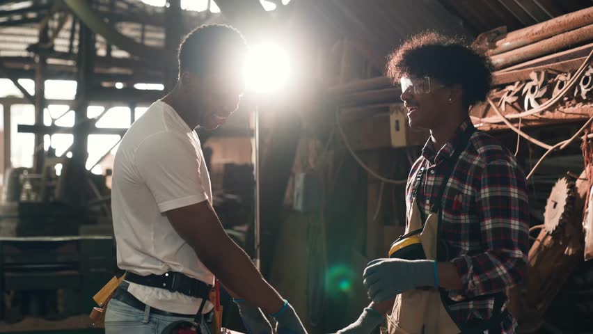 African American Foreman And Carpenter Worker Collaborate In Sawmill Wood Factory, Showcasing Skilled Teamwork And Construction Expertise In An Industrial Workshop Environment