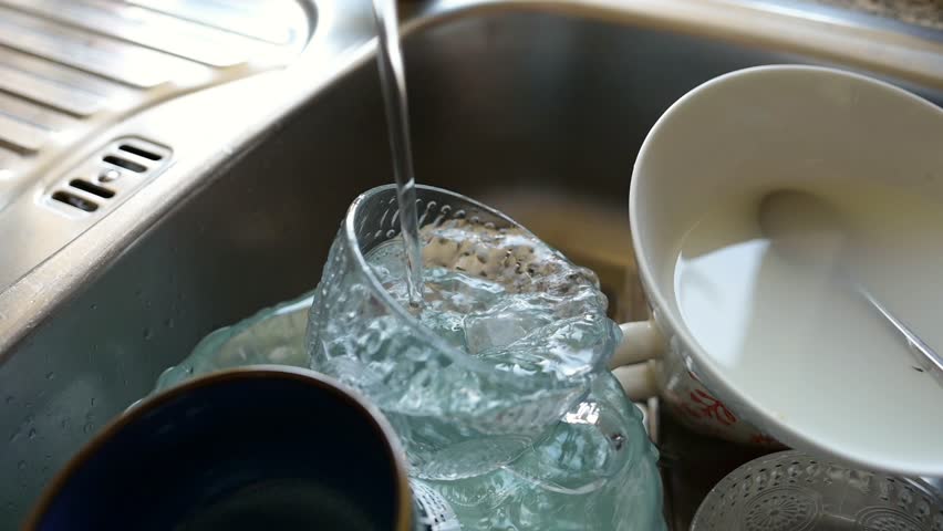 A close-up shot of running water pouring directly into dirty dishes in the sink.