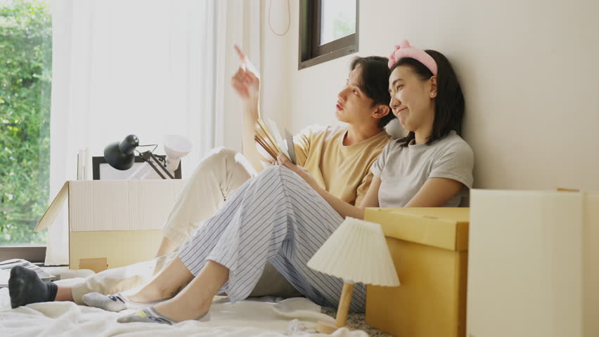 Attractive pair renovating after relocation. Two people select floor and wall patterns from catalog. The enjoy of moving, redecorating, and creating a new home environment together.