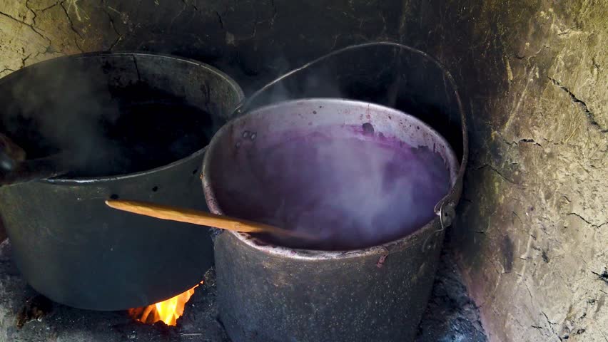 Two blackened pots boiling over open fire, filled with purple colored water and alpaca wool in a traditional Quechua dyeing process in Sacred Valley