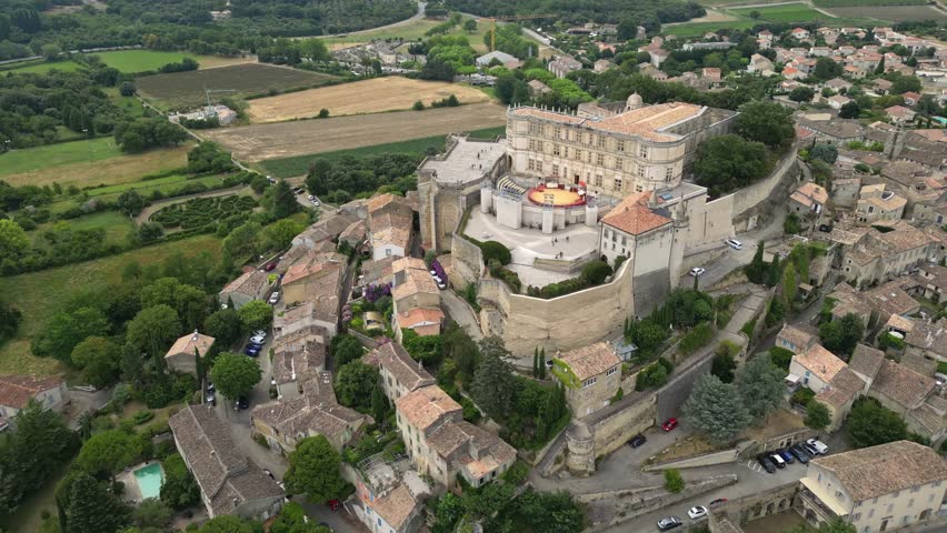 Aerial drone view of Grignan Castle surrounded by lush greenery and historic village in Provence, France – medieval fortress with scenic landscape and vibrant natural surroundings
