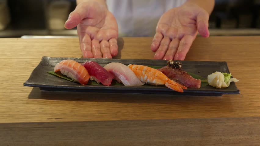 A sushi chef presents his beautifully plated fresh nigiri sushi with 5 different types and flavours with a side of pickled ginger.