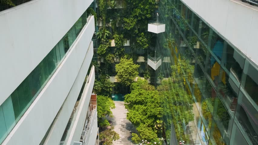 Modern shopping mall courtyard with lush vertical garden and and green tropical plants in Bangkok city surrounded by glass walls, Thailand. Green architecture and sustainable design in retail 