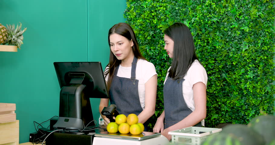 Asian and Caucasian LGBTQ couple standing together smiling while operating fruit shop point of sale preparing tropical grocery store before opening business