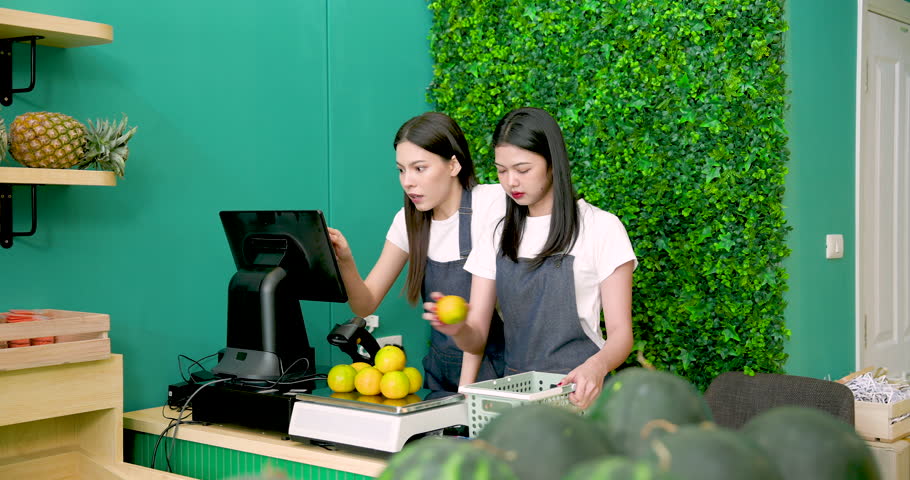 Asian LGBTQ partner standing beside smiling Caucasian co-owner preparing fruit counter together at tropical grocery shop before store opens in morning