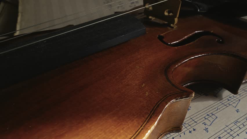 Aged violin with missing string lays on sheet music SLIDE reveal close-up