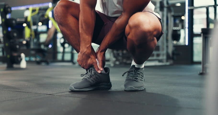 Legs, feet and man with ankle pain in gym, fitness injury or muscle tension with pressure. Hands, sneakers and athlete with massage for fracture, sprain or joint ache with intense exercise at center