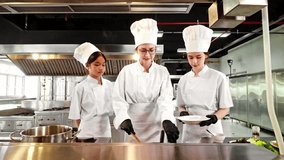 Chef instructor guides two young culinary students in plating pasta during a professional cooking class in a commercial kitchen, emphasizing hands-on learning, food preparation, and teamwork skills. - Powered by Shutterstock - Get 15% off with code: PIKWIZARD15