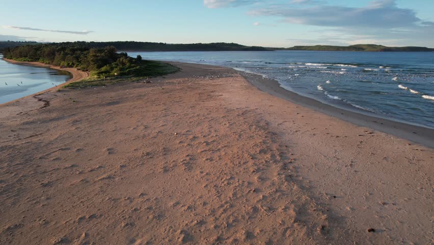 Aerial view of the coastal horizon with hills, a sandy shoreline, and birds flying over the water at Praia da Amoreira, Portugal. A scenic and peaceful beach landscape
