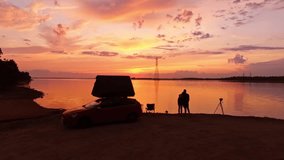 Golden lake sunset with couple hugging by car tent, camera on tripod nearby - Powered by Shutterstock - Get 15% off with code: PIKWIZARD15