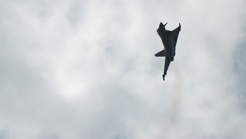 Silhouette of military jet fighter flying above in the sky with clouds in the background in slow motion