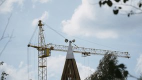 Weathervane made of hemispheres spins on roof of decorative building against backdrop of tower crane and daises. Visual demonstration of strength and direction of wind in cloudy weather. - Powered by Shutterstock - Get 15% off with code: PIKWIZARD15