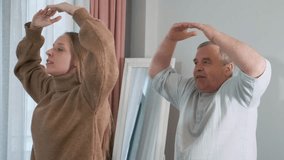 Adult daughter teaching her elderly father practicing slow balance exercises indoors with arms stretched out. Wellness at home, family support, senior fitness, healthy lifestyle, active seniors - Powered by Shutterstock - Get 15% off with code: PIKWIZARD15