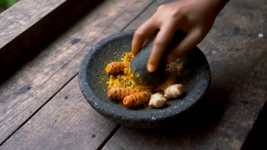 Person grinding fresh turmeric in stone mortar and pestle.
