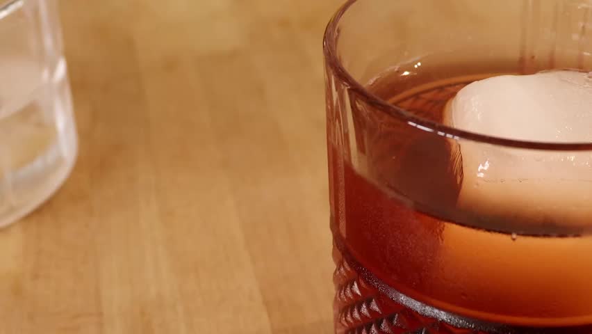 Close-up of a homemade drink. Old Fashioned cocktail with two maraschino cherries at the bottom and ice in an elegant glass. Dark amber color.